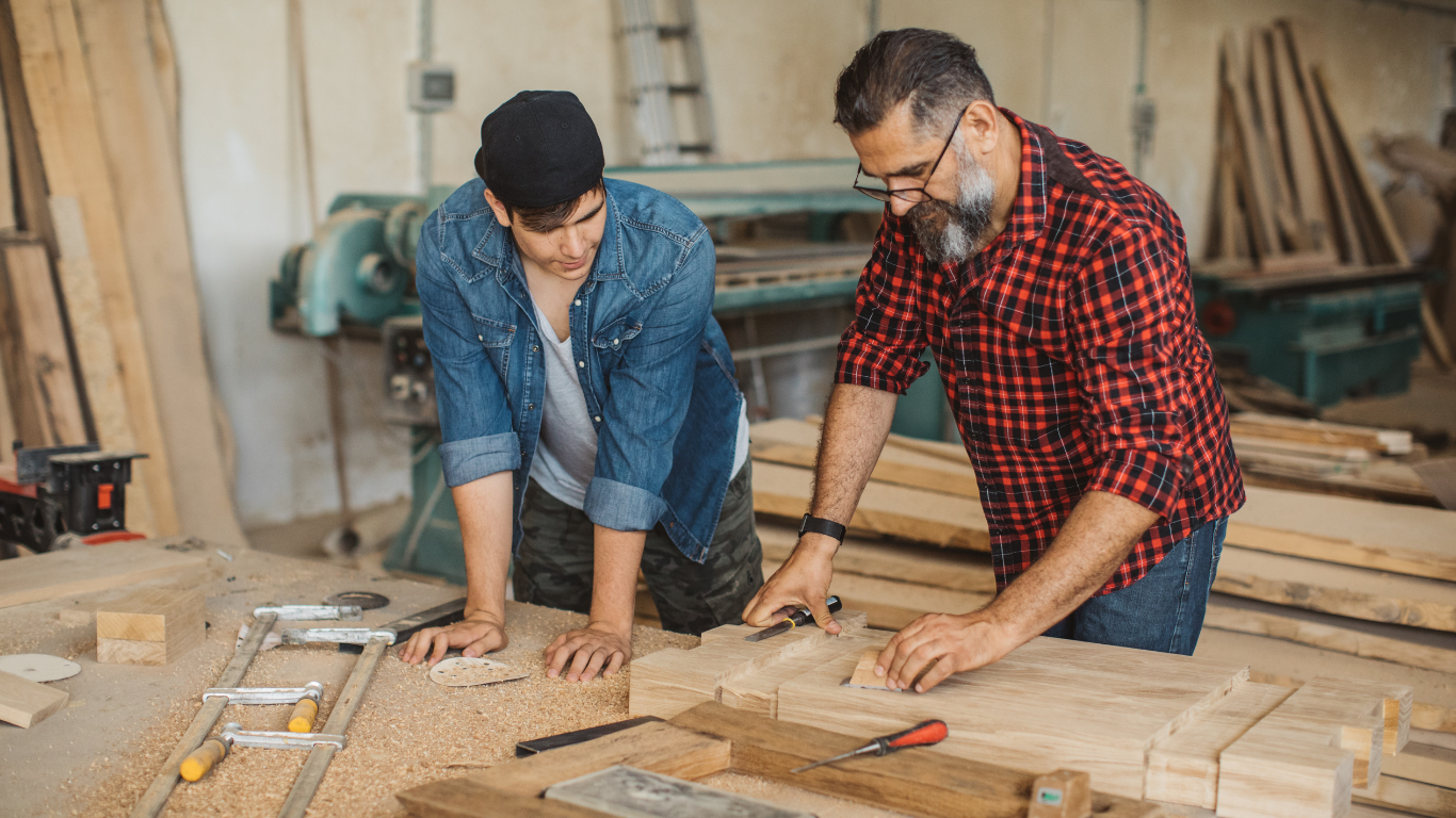 Young man learning carpentry from older man.